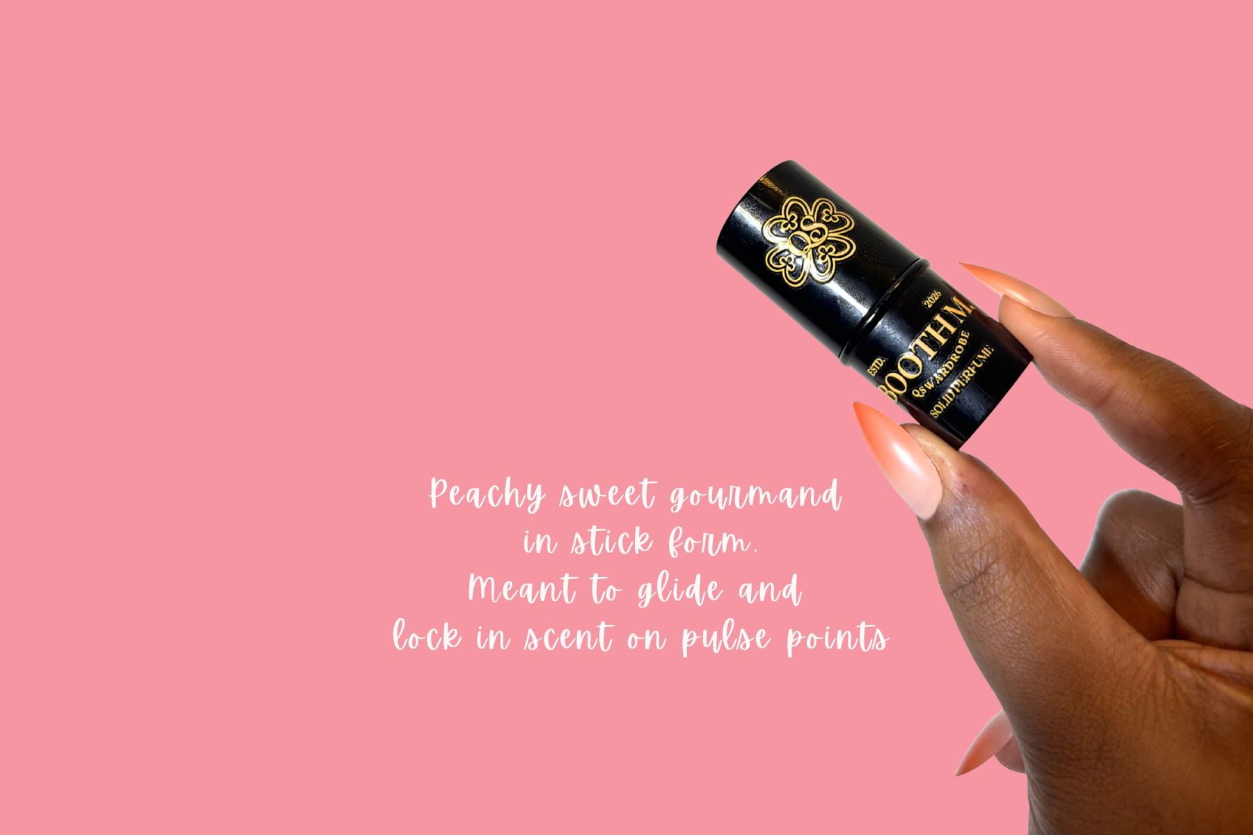 Hand holding a black stick product with gold text on a pink background